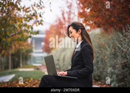Erfolgreiche japanische Frau bei der Arbeit mit ihrem Laptop im Freien, Konzept der Gleichberechtigung und Gleichberechtigung für Frauen, Geschäftsmann, Online-Handel, positiv Stockfoto