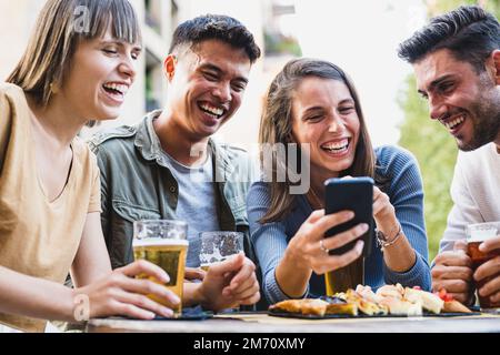 Gruppe von Freunden im Pub, Leute, die Spaß haben und Smartphones verwenden, um Essen und Getränke zu fotografieren, glückliche Schüler, die die App nutzen, um Inhalte in Sozia zu teilen Stockfoto