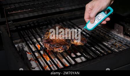 Prüfen der sicheren Lebensmitteltemperatur mit einem digitalen Sofortthermometer. Kochen Sie die Temperatur des frisch gegrillten Steaks auf dem heißen Grill. Stockfoto