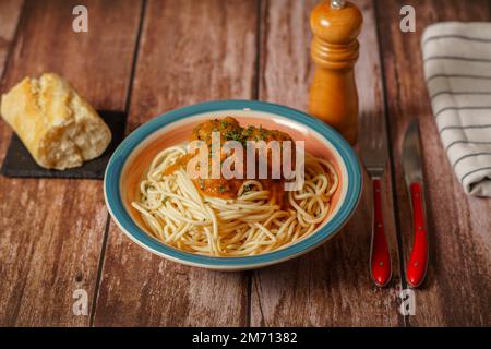 Teller mit Fleischbällchen mit Spaghetti mit Besteck und Brot- und Pfefferstreuer auf einem Holztisch Stockfoto