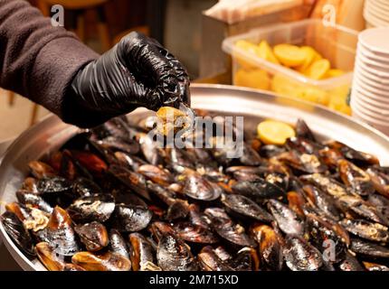 Street Flavors Gefüllte Muscheln. Hand-Muscheln. Ein Haufen schwarzer Schalentiere. Stockfoto