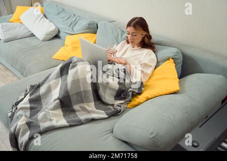 Kranke junge Frau, eingewickelt in Karo, die sich auf die Einnahme von Medikamenten vorbereitet Stockfoto