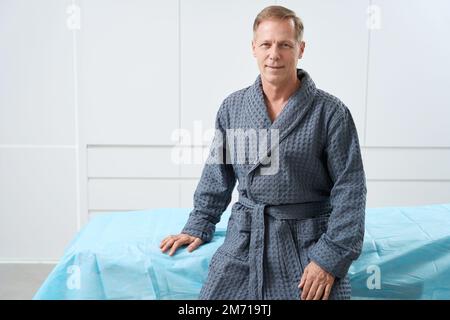 Lächelnder Patient mittleren Alters sitzt auf dem Bett Stockfoto