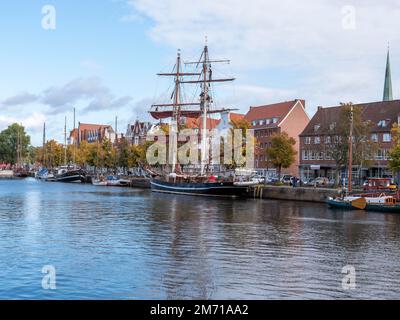Historische Segelschiffe am Ufer des Flusses Trave und dahinter die Backsteingebäude Alte Hansestätte im UNESCO-Weltkulturerbe Stockfoto