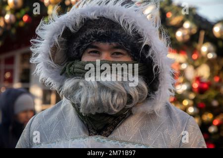 Moskau, Russland. 6. Januar 2023. Ein yakut-Mann im nationalen Winterkostüm ist auf dem Weihnachtsmarkt auf dem Manezhnaya-Platz im Zentrum von Moskau, Russland, vor dem Hintergrund eines Weihnachtsbaums zu sehen. Die Temperatur in Moskau fiel auf 22 °C (7,6 °F) Stockfoto