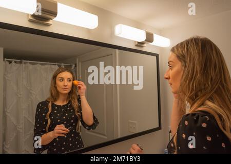 Ein Mädchen, das in den Spiegel schaut, während es sich im Bad schminkt Stockfoto