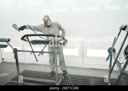 Ein Mann in einem Atemschutzgerät, der die Farbe von Autoteilen restauriert Stockfoto