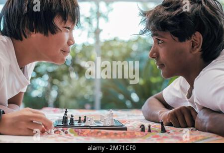 Zwei Jungen indischer und chinesischer Herkunft starren sich beim Schachspiel in die Augen. Wettbewerbsbegriff und Rassenvielfalt. Stockfoto