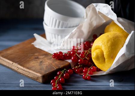 Frisch gekaufte Zitronen und rote Johannisbeeren in Papiertüte und weiße Gratiniergerichte Stockfoto