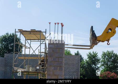 Auf einer Baustelle wird ein Gabelstapler mit Ausleger zum Entladen von Betonblöcken eingesetzt, die auf Paletten geladen werden. Stockfoto