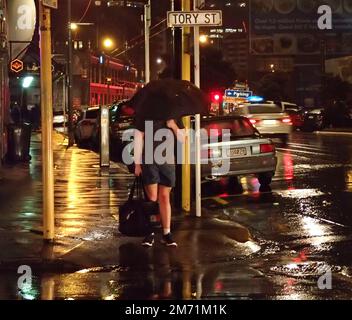 Ein Mann in Shorts und T-Shirt, der am Kreuz wartet, an einer kalten und nassen Winternacht in Wellington, Neuseeland Stockfoto