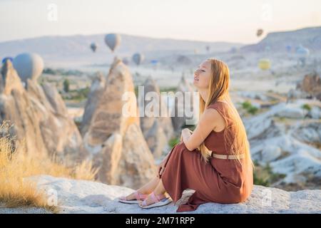 Eine Touristin, die Heißluftballons in Kappadokien, Türkei, ansieht. Happy Travel in Turkey Concept. Eine Frau auf einem Berggipfel, die eine wunderbare Aussicht genießt Stockfoto
