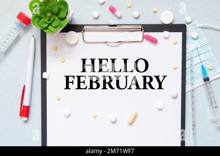 Auf dem Tisch liegt eine Holztafel mit der Aufschrift "HALLO FEBRUAR". Blick von oben. Flach verlegt. Marketingkonzept. Stockfoto