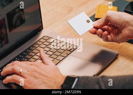 Nahaufnahme von männlichen Händen mit weißer, unbeschrifteter Kreditkarte und Tippen. Online-Shopping oder Bezahlung. Stockfoto