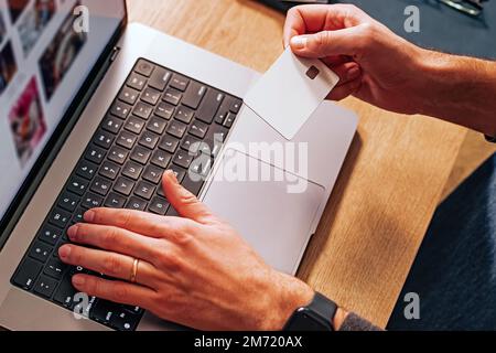 Nahaufnahme von männlichen Händen mit weißer, unbeschrifteter Kreditkarte und Tippen. Online-Shopping oder Bezahlung. Stockfoto