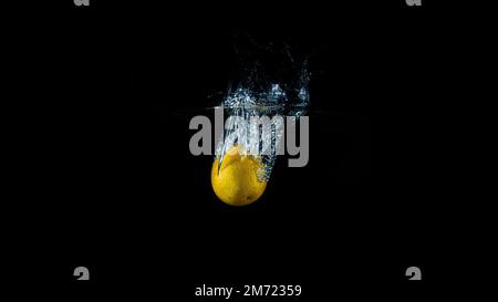 Frische, ungeschälte Orangentropfen in klares Wasser, minimalistischer schwarzer Hintergrund, keine Menschen Stockfoto