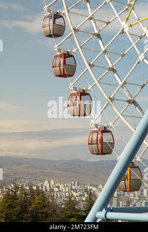 Riesenrad mit bunten Kabinen vor einer atemberaubenden spektakulären Aussicht auf Tiflis Stockfoto