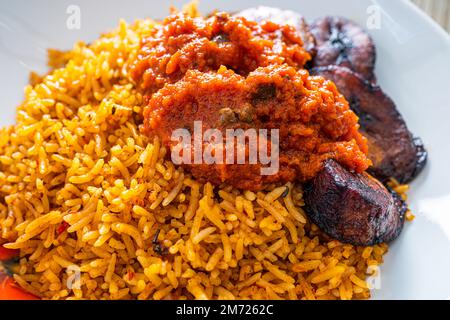 nigerianischer Jollof Reis serviert mit Plantain und Eintopf Stockfoto