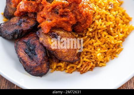 nigerianischer Jollof Reis serviert mit Plantain und Eintopf Stockfoto