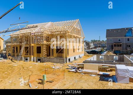 Der Kran hält Holzbalken, da er Dachsparren auf einem unfertigen Holzhaus installiert, das noch im Bau ist. Stockfoto