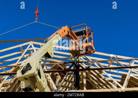 Während des Baus von Sparren hält ein unfertiger Holzhauskran Holzbalken auf dem Dach Stockfoto