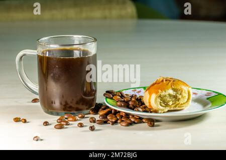 Ein Glas gebrühten Kaffee in einem durchsichtigen Glas aus Glas und ein Stück Kuchen auf einem kleinen Teller, Kaffeepausen-Konzept, um Spannung abzubauen Stockfoto