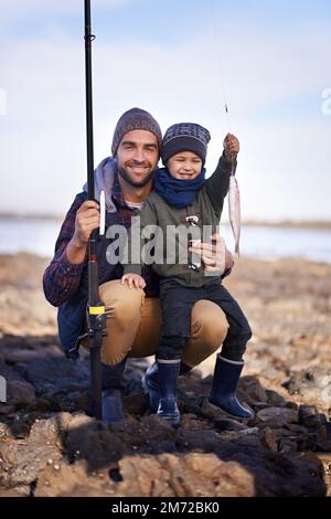 Fang jeden an. Porträt eines süßen kleinen Jungen, der den Fisch hält, den er mit seinem Vater gefangen hat. Stockfoto