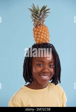 Lass uns tropisch werden. Ein kurzer Blick auf einen jungen afrikanischen Teenager mit einer Ananas auf dem Kopf im Studio. Stockfoto