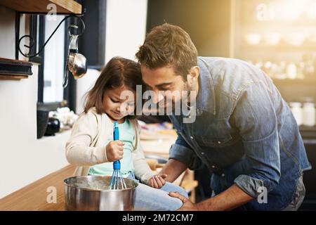 Lernen durch Handeln. Ein Vater und eine Tochter, die zusammen Pfannkuchen machen. Stockfoto