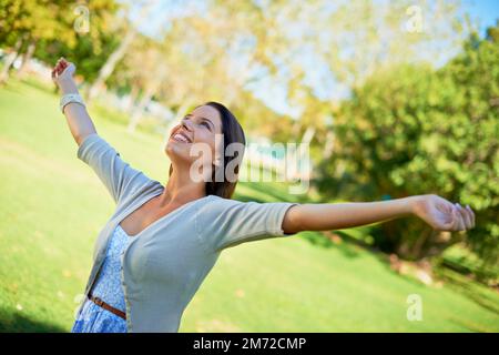 Ich fühle mich frei. Eine sorglose junge Frau, die einen Tag im Park genießt. Stockfoto