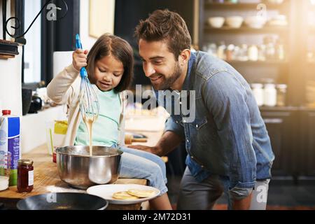 Ich zeige Dad ein oder zwei Dinge über Kochen. Ein Vater und eine Tochter, die zusammen Pfannkuchen machen. Stockfoto