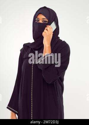 Modern trifft Tradition. Studioporträt einer jungen muslimischen Frau, die mit einem Handy spricht. Stockfoto