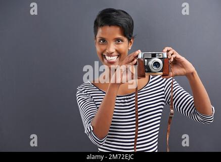 Sagen Sie Cheese. Porträt einer glücklichen jungen Frau, die auf grauem Hintergrund steht. Stockfoto