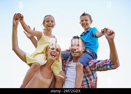 Eine Familie, die weiß, wie man Viel Spaß. macht Ein kleines Porträt von zwei glücklichen Eltern, die ihre kleinen Kinder auf den Schultern tragen. Stockfoto