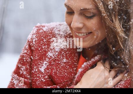 Liebe den ersten Schneefall. Eine attraktive Frau, die sich draußen im Schnee genießt. Stockfoto