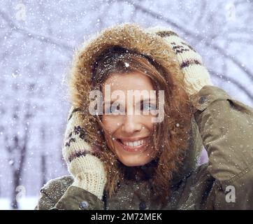 Liebe den ersten Schneefall. Eine attraktive Frau, die sich draußen im Schnee genießt. Stockfoto