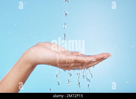 Hand, Wasser und Hydratation mit einer Frau, die im Studio auf blauem Hintergrund für Hygiene oder Körperpflege putzt. Wasserspritzer, Gesundheit und Hautpflege mit einem Stockfoto