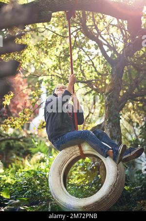 Das ist die ursprüngliche playstation. Ein junger Junge, der im Garten auf einer Reifenschaukel schwingt. Stockfoto