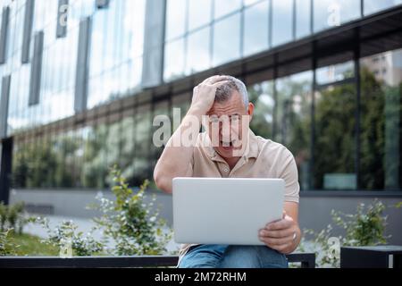 Geschriener, gestresster, erwachsener, älterer, grauhaariger Geschäftsmann mit Hand-am-Kopf-Laptop, Wireless-Technologie. Verlorenes Geld Stockfoto