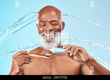 Gesicht, Wasserspritzer und schwarzer Mann mit Zahnbürste und Zahnpasta im Studio isoliert auf blauem Hintergrund. Zahn-, Mundhygiene und männliches Seniorenmodell mit Stockfoto