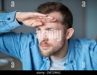 Attraktiver, freiberuflicher Software-Ingenieur mit Bart am Arbeitsplatz im Büro, der sich auf neue Möglichkeiten mit Computer im Hintergrund freut. Hand nahe der Stirn Stockfoto