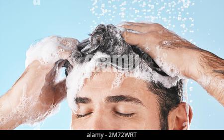 Gesicht, Wasserspritzer und Shampoo-Dusche eines Mannes im Studio isoliert auf blauem Hintergrund. Wassertropfen, Haarpflege und waschen männlicher Modelle, Baden oder Stockfoto