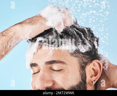 Gesicht, Wasserspritzer und Mann in der Dusche mit Shampoo im Studio auf blauem Hintergrund. Hautpflegedermatologie, Wassertropfen und männliche Modellreinigung, Baden Stockfoto