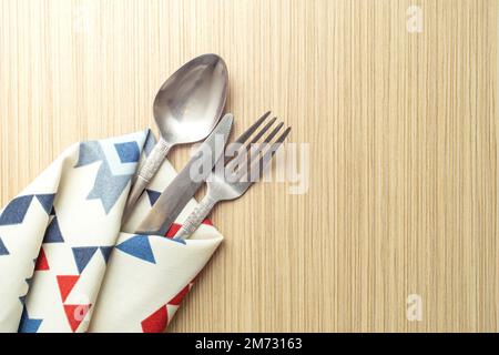 Esstisch mit Löffelgabel und Messer in gemusterter Stoffserviette auf Holztisch Stockfoto