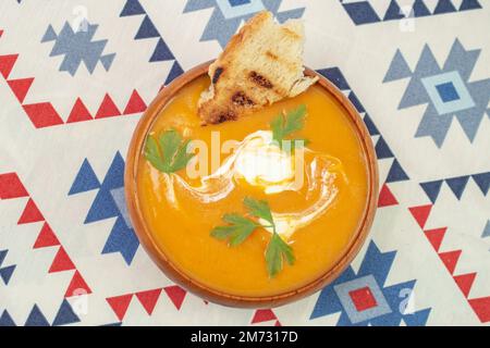 Kürbissuppe mit Petersilienblättern, saurer Sahne und getoastetem Brot in einer Holzschüssel, weicher Fokus Nahaufnahme Stockfoto