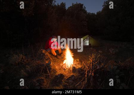 Ein Mann sitzt nachts neben dem Lagerfeuer in Sizilien, Ätna Park, Italien Stockfoto