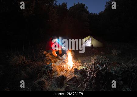 Ein Mann sitzt nachts neben dem Lagerfeuer in Sizilien, Ätna Park, Italien Stockfoto