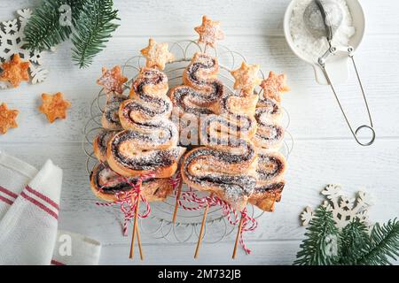 Weihnachtsbaumförmige Blätterkuchen mit Schokoladenfüllung, Zuckerpulver und Lutscher auf altem, weißem Holzhintergrund. Weihnachten, Neujahr, Appetit Stockfoto