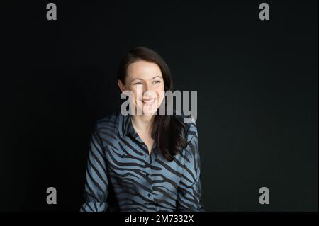 Porträt einer aufrichtig lächelnden, reifen Frau auf schwarzem Hintergrund Stockfoto