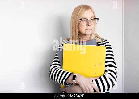 Reife, aufmerksame Geschäftsfrau, die Ordner isoliert auf hellem Hintergrund hält Stockfoto